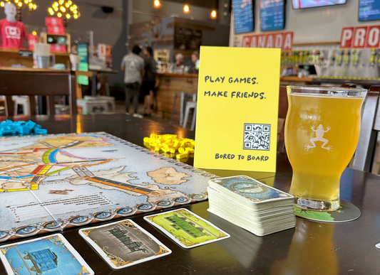 Board game setup with a glass of beer and a sign encouraging play and friendship.